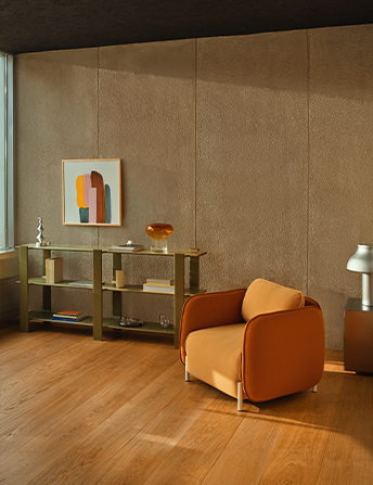 Orange Linka armchair in a modern interior with a wooden floor and textured wall, next to an olive Ligo shelf with decorations and a painting.