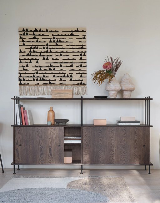 Bava wooden half bookcase with sliding doors and a metal frame beneath a decorative wall hanging