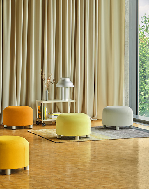 Colourful poufs in shades of yellow and grey arranged in a modern interior with large windows and curtains