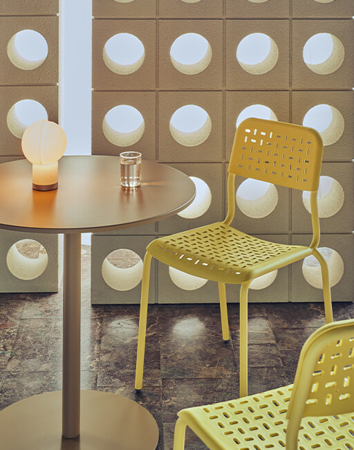 Perforated yellow Tube plastic chairs at a round table against a sculptural wall