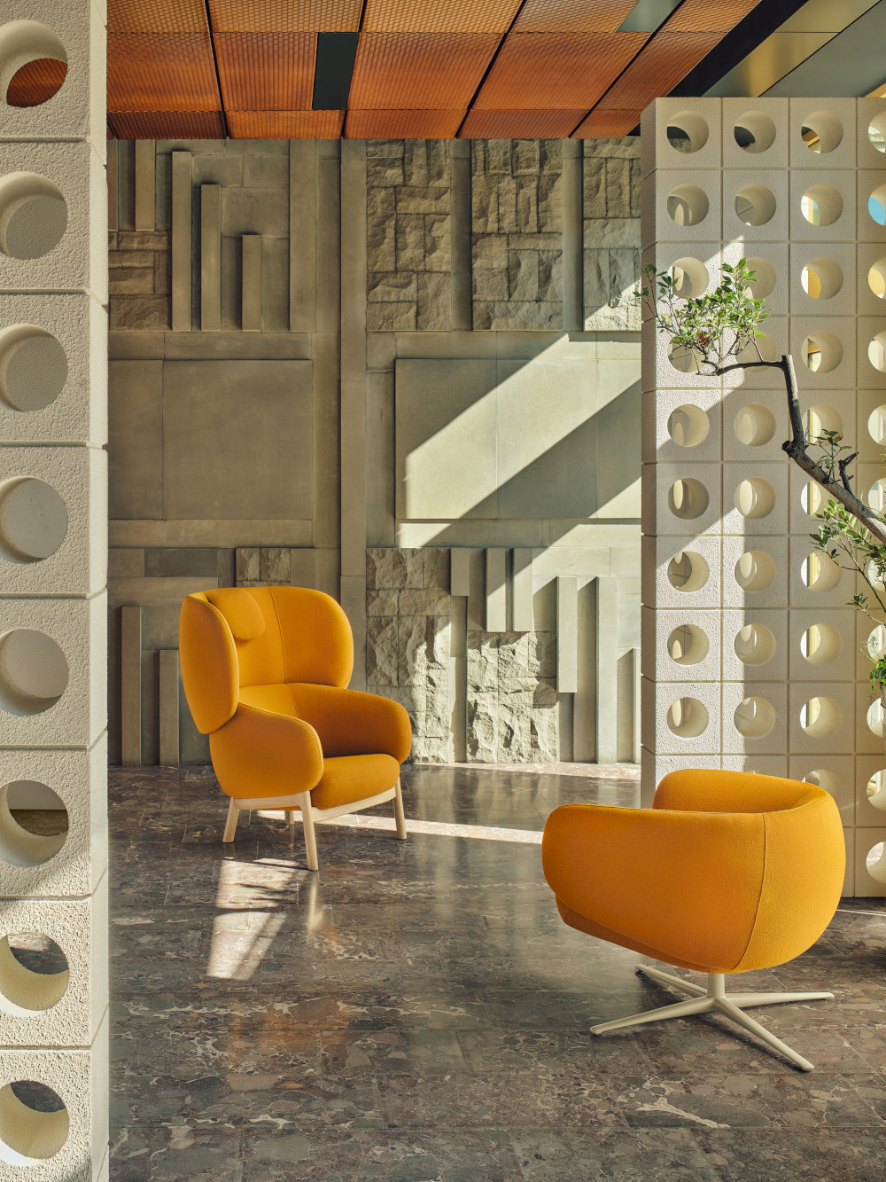 A high and low Grand Grace armchair arranged by a sculptural wall