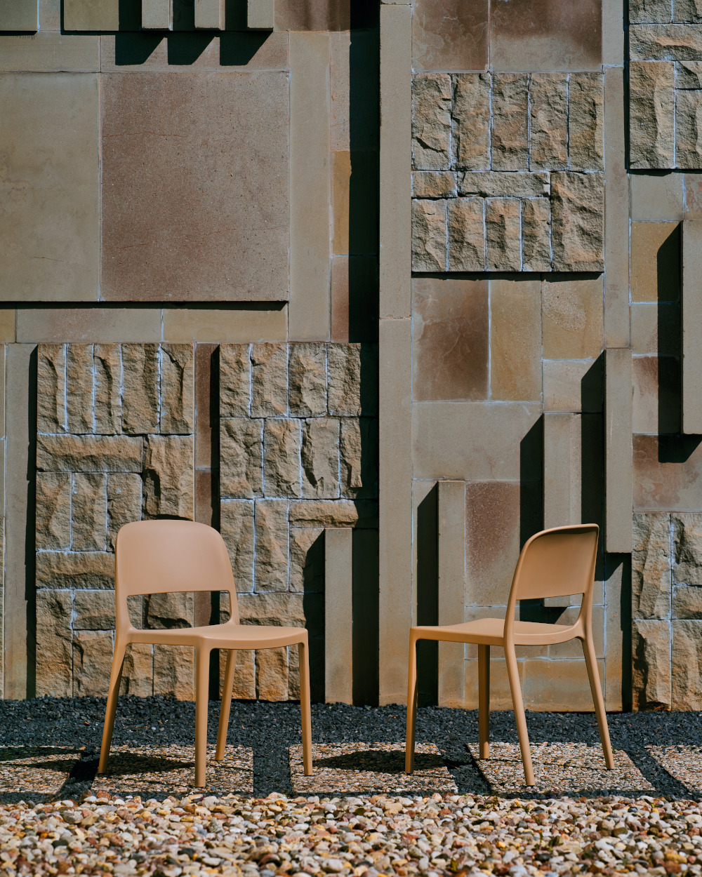 Two brown plastic chairs outside, a sculptural stone wall behind them